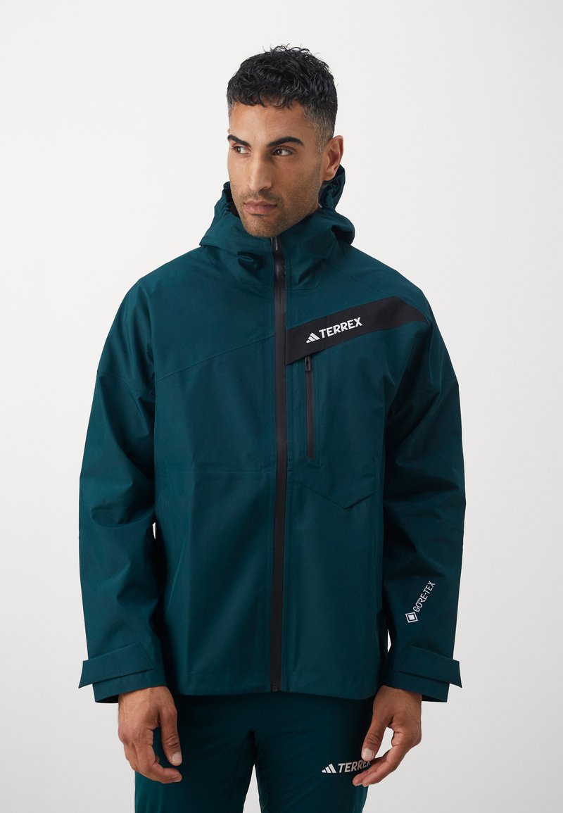Dark teal waterproof jacket with a black shoulder panel and logo. Features a hood, front zipper, and adjustable cuffs for a secure fit.