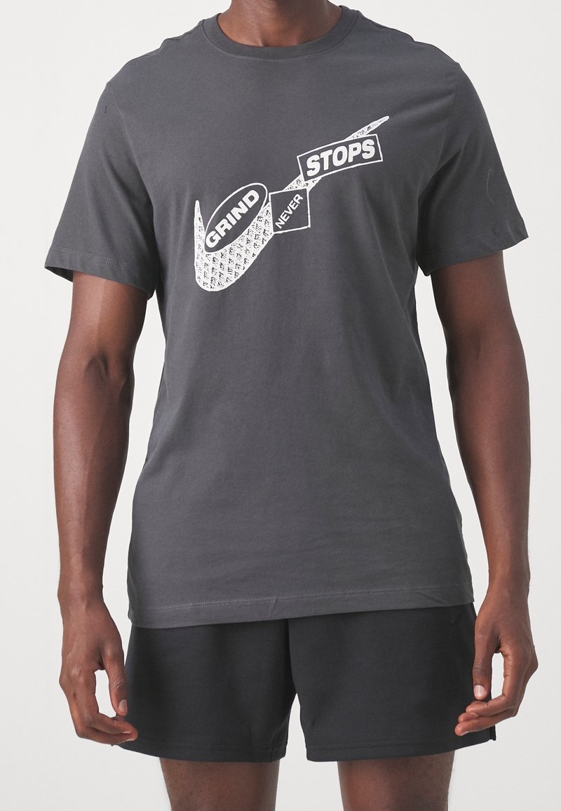 Tummanharmaa puuvillapaita, jossa on valkoinen grafiikkasuunnittelu ja teksti. Lyhyet hihat ja pyöreä kaula-aukko. Pehmeä rakenne, normaali istuvuus.