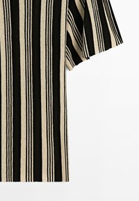Short-sleeved shirt with vertical black and beige stripes, shown from the side and cropped at the shoulder against a plain background.