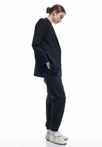 Schwarze, maßgeschneiderte Blazer mit einer lässigen Passform, kombiniert mit passenden Jogginghosen. Weiße Sneakers runden das Outfit ab.