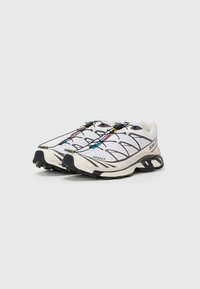 Scarpe da trail running con tomaia in rete bianca, accenti viola e suola in gomma nera. Presentano un colorato sistema di allacciatura e motivi testurizzati sui lati.