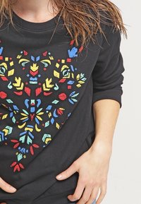 Sudadera negra con un diseño floral colorido que presenta formas rojas, azules, amarillas y verdes. Mangas largas y un escote redondo.