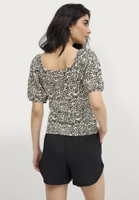 Kort liefde top in beige met zwarte luipaardvlekken, met een ronde rug en gerimpelde pofmouwen, gecombineerd met zwarte textured shorts.