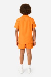 Oranje shirt met korte mouwen en bijpassende korte broek van lichtgewicht stof. Witte sneakers en witte sokken op crew-lengte maken de look compleet.