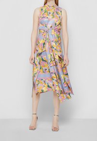 Robe sans manches à motif floral dans des couleurs pastel, avec ceinture à nouer et ourlet asymétrique. Confectionnée en tissu léger avec un design superposé et fluide.