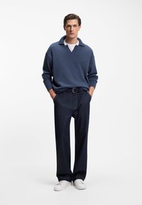 Blue knit sweater with a V-neck and short collar, paired with dark denim straight-leg pants and white sneakers.