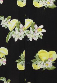 Tissu noir avec fermeture à boutons présentant un motif de tranches de citron jaunes, feuilles vertes et fleurs blanches avec accents roses.