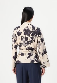 Top avvolgente con fantasia floreale in beige e grigio scuro, dotato di maniche lunghe, cintura in vita e orlo a peplum. Tessuto liscio con una texture leggera.