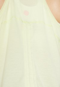 Light yellow sleeveless top with soft texture, featuring a central seam and a light pink circular accent at the neckline.