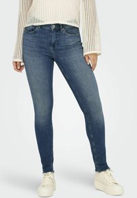 Vaqueros de denim azul ajustados con un ligero desgaste, diseño de cinco bolsillos y dobladillo deshilachado. Combinados con zapatillas blancas de textura y una camiseta de punto suelta.