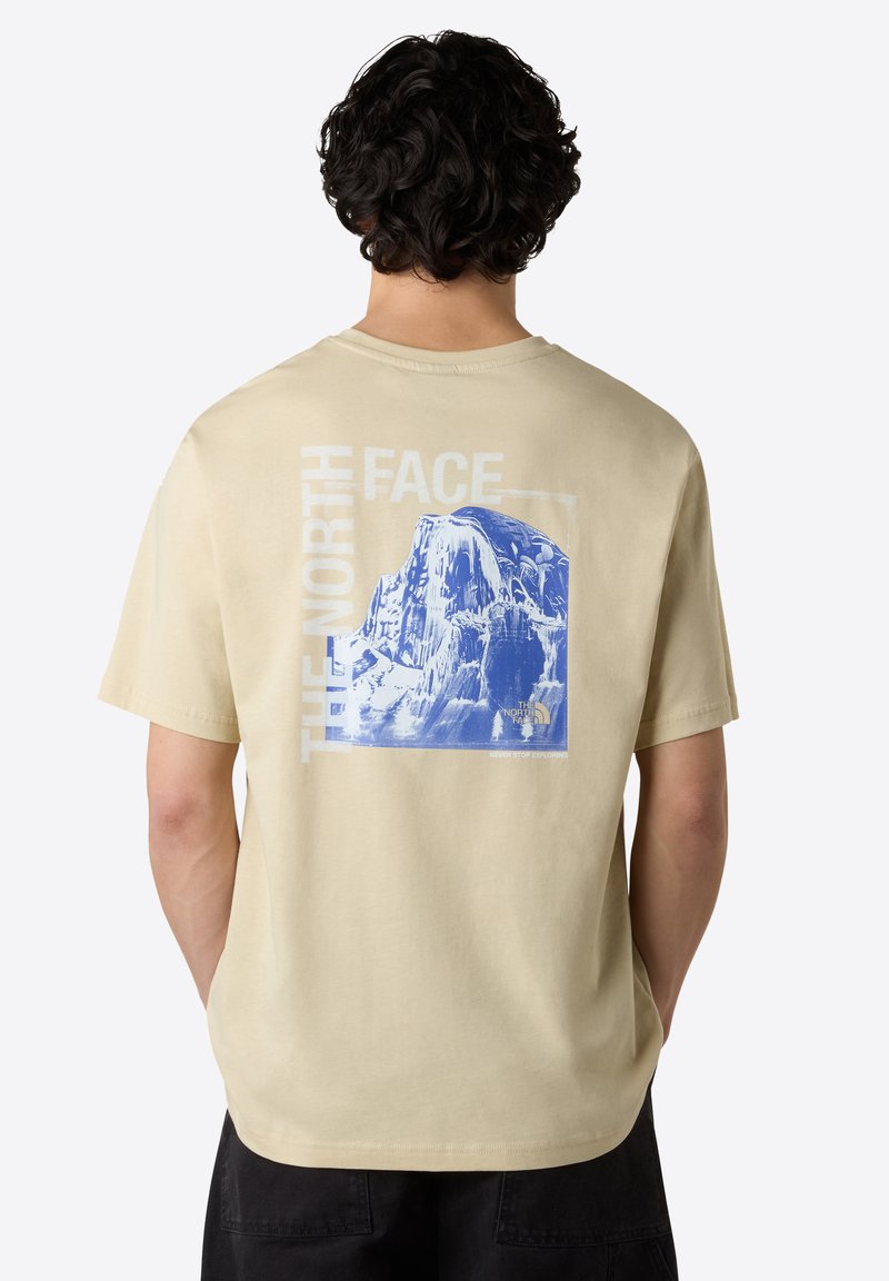 Béžové bavlněné tričko s modrou grafikou hory a textem "THE NORTH FACE". Krátké rukávy, volný střih a kulatý výstřih.