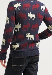 Maglione blu navy con un motivo di sagome di alci rosse e bianche. Polsini e orlo a coste, texture a maglia e scollo rotondo.