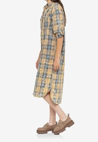Abito camicia lungo, con bottoni, in fantasia tartan che presenta tonalità di giallo, blu e beige. Realizzato in tessuto leggero, con maniche arrotolate e spacchi laterali.