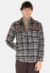 Giacca di flanella a scacchi in nero, bianco e marrone con un colletto in velluto a coste color beige e tasche sul petto. Texture morbida, chiusura con bottoni e maniche lunghe.