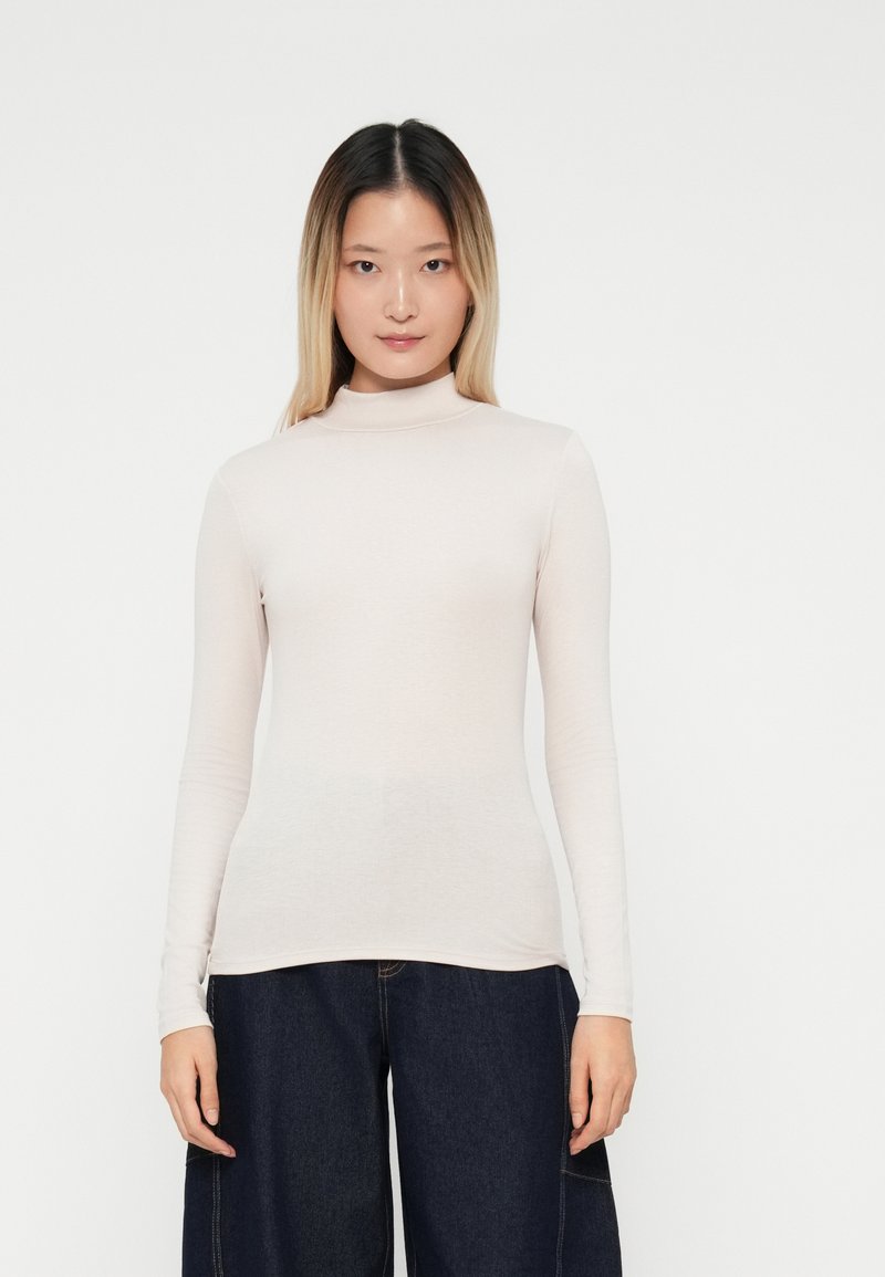 Haut col roulé à manches longues de couleur rose clair, fabriqué en tissu doux et extensible. Design ajusté avec une texture lisse, associé à un jean large bleu foncé.