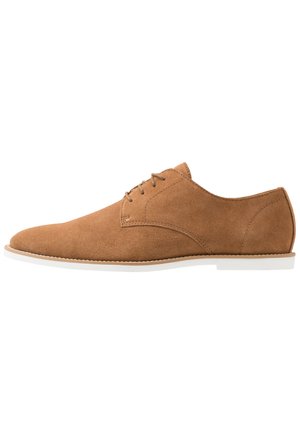 Chaussure habillée pour homme en daim marron clair avec lacets et semelle blanche, présentée de profil sur un fond blanc.