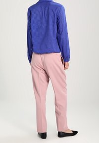 Camicia blu a pois con maniche lunghe, abbinata a pantaloni rosa e ballerine nere, vista da dietro. Tessuto morbido e vestibilità sartoriale.