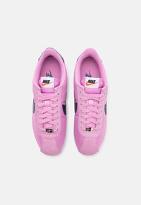 Pink Nike sneakers with a suede and mesh upper, round toe, lace-up front, and navy accents. Features a branded tongue and textured sole.