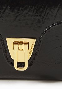 Black patent leather handbag with a glossy finish, featuring a gold-tone clasp and embossed logo. Smooth texture with rounded edges.