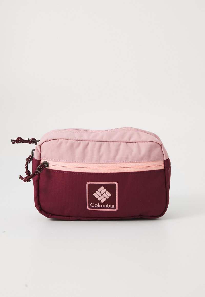 Columbia torbica u bordo i svijetloružičastoj boji, s glatkom teksturom, zatvaranjem na patentni zatvarač i logotipom brenda sprijeda. Kompaktni dizajn.