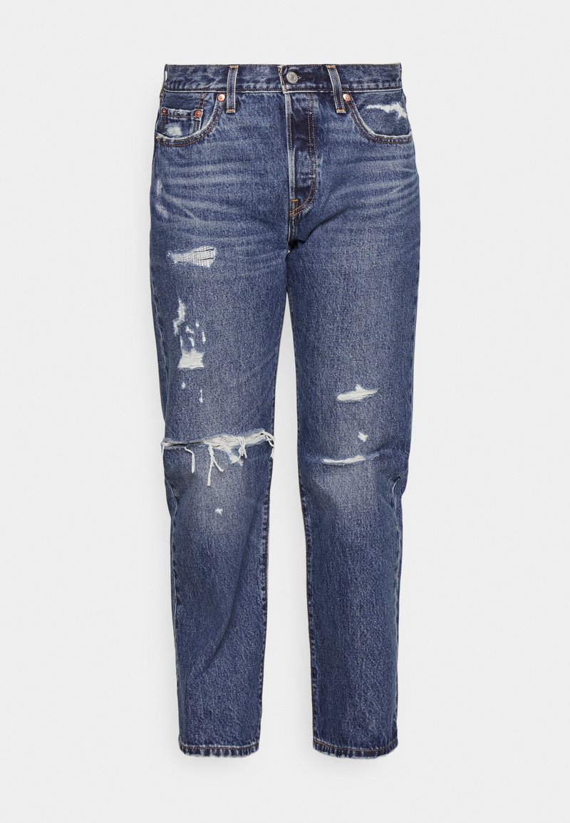 Vaqueros de denim azul con un ajuste relajado, que presentan áreas desgastadas y dobladillos deshilachados. Diseño clásico de 5 bolsillos con acentos de metal.