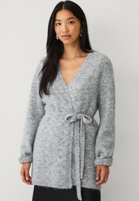 Cardigan avvolgente grigio realizzato in un morbido materiale testurizzato. Presenta un cintura da legare in vita, maniche lunghe e scollatura a V.