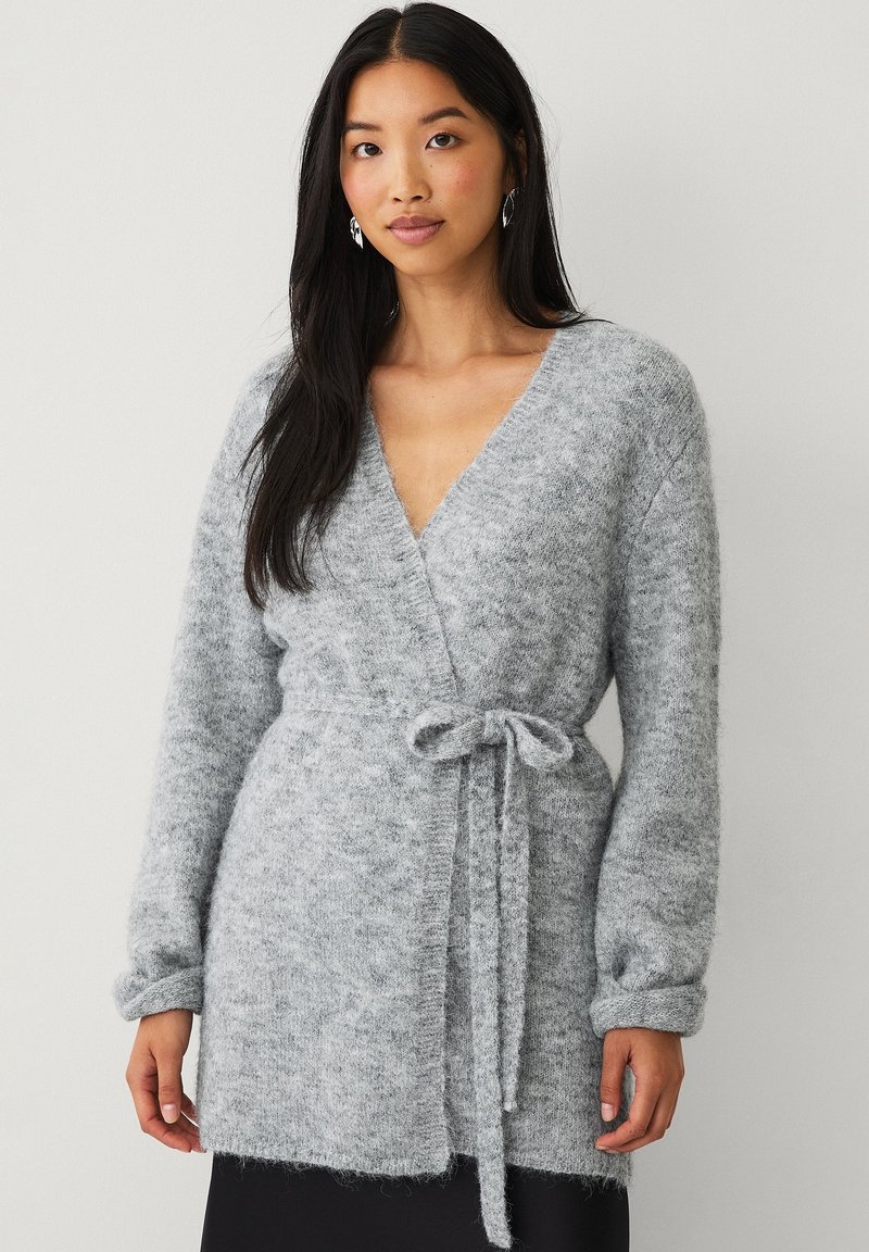 Cardigan avvolgente grigio realizzato in un morbido materiale testurizzato. Presenta un cintura da legare in vita, maniche lunghe e scollatura a V.