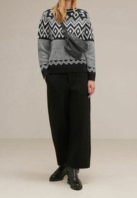 Stickad tröja med ett geometriskt mönster i svart och grått, hög halsringning, i kombination med vida svarta byxor och svarta anklarstövlar.