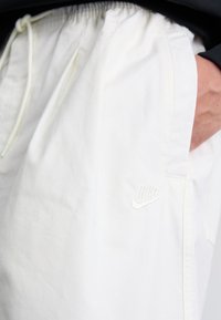 Hvide shorts med elastisk talje, en hånd i lommen, og et lille hvidt Nike-logo på venstre side.