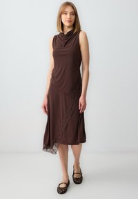 Abito senza maniche color marrone con scollo a cappuccio drappeggiato, caratterizzato da un dettaglio in pizzo lungo il lato inferiore. Tessuto morbido con una forma fluida.