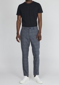 Černé tričko s kulatým výstřihem spojené se šedými kostkovanými kalhotami s knoflíkovým zapínáním. Celkový vzhled doplňují bílé tenisky.