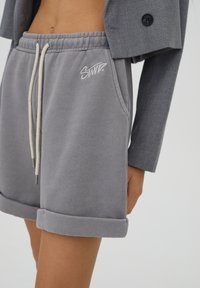 Shorts in cotone grigio misto con orli arrotolati, vita elastica e cordini avorio con logo ricamato sulla parte anteriore.