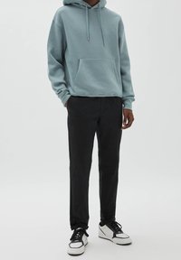 Světle modrá bavlněná mikina s kapucí s přední kapsou, volný střih, kapuce se šňůrkou; doplněná černými kalhotami a bílými teniskami s černými detaily.