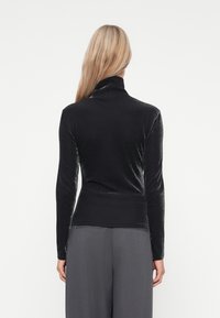 Μαύρο μακρυμάνικο πουλόβερ με τρυπητό γιακά και λείο, γυαλιστερό υλικό. Κομψός σχεδιασμός, με ψηλό γιακά και ελαφρώς καμπυλωτό στρίφωμα.