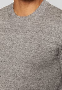 Grå stickad tröja med rund halsringning, med en mjuk textur och subtila variationer i stickmönstret.