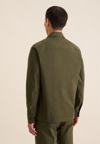 Veste cintrée vert olive avec un col plat, des poignets boutonnés et une texture lisse et mate. Design à dos droit avec des lignes épurées.