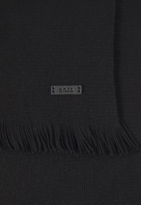 Sort strikket tørklæde med frynser i kanten og rektangulær form. En lille, præget "BOSS" label er syet fast til stoffet.