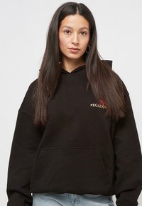 Black hoodie with a front pocket and a small embroidered "PEGADOR" logo in red and gold. The fabric appears soft, with a relaxed fit.