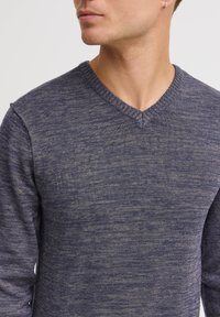 Maglione a V in tinta unita, realizzato in tessuto a maglia testurizzato. Presenta maniche lunghe e collo a costine. Motivo heathered sottile su tutta la superficie.
