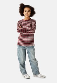 Red and gray striped long-sleeve shirt with round neckline, paired with light blue baggy jeans and white sneakers. Crossed arms pose.