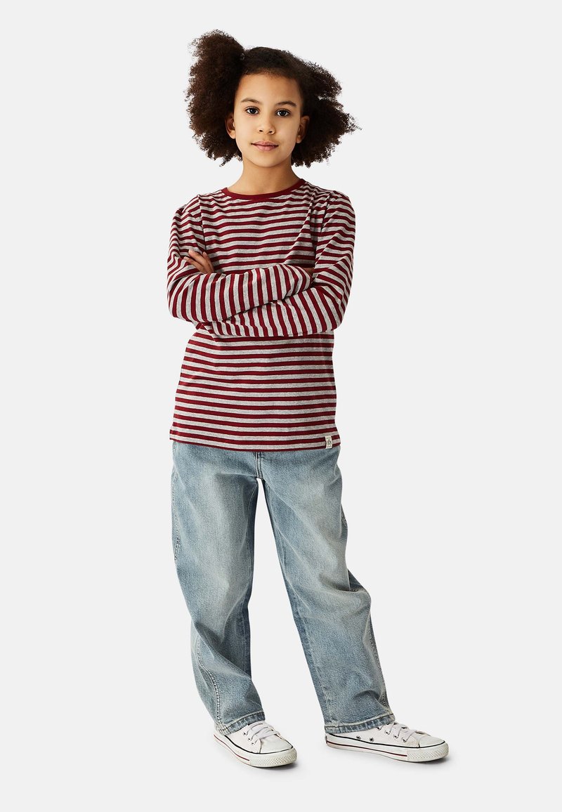 Red and gray striped long-sleeve shirt with round neckline, paired with light blue baggy jeans and white sneakers. Crossed arms pose.