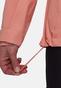 Helle Korallenjacke mit strukturiertem Finish, ausgestattet mit einem Kordelzug an der Taille und elastischen Bündchen für eine anpassbare Passform.