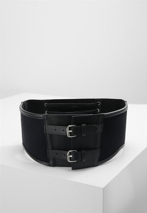 Ampia cintura nera in vita con due fibbie regolabili argento e lati elastici, esposta su una superficie bianca.