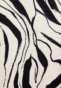 Tissu à imprimé zèbre noir et blanc avec une surface texturée. Des lignes ondulées créent un motif audacieux sur un fond crème.