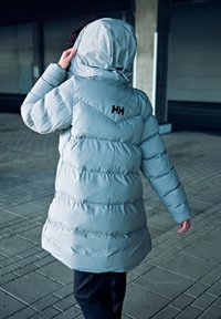 Grijze pufferjack met een capuchon, voorzien van een chevron quiltpatroon en een zwart logo op de achterkant. Soepele stof en geïsoleerd ontwerp.