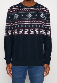 Mörkblå stickad tröja med vita och vinröda vintermönster, inklusive snöflingor och renar, med kabelstickad textur.