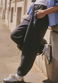 Grå sweatpants med en avslappnad passform och sidofickor, kombinerade med glänsande silverfärgade sneakers. Byxorna har ett broderat "self."-detalj.