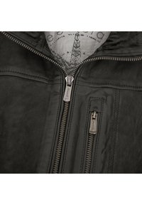 Schwarze Lederjacke mit metallischen Reißverschlüssen. Merkmale sind eine glatte Textur, kontrastierende Nähte und ein hellgraues Innenfutter mit Druck.