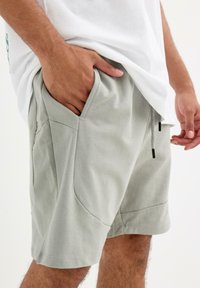 Pantalones cortos de color gris claro con cinturilla ajustable, bolsillos frontales y textura suave, diseñados para la comodidad y facilidad de movimiento.
