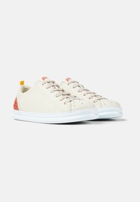 Ein Paar off-white Low-Top-Sneaker mit weißen Sohlen, roten Akzenten an Ferse und Zunge sowie gesprenkelten Schnürsenkeln vor einem einfarbigen Hintergrund.